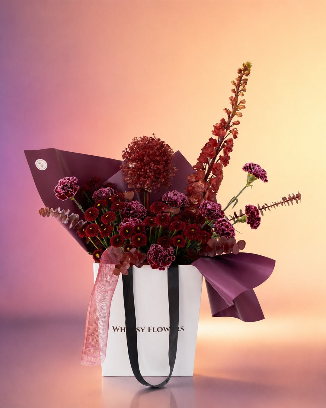 Maroon Melody flower bag arrangement with deep burgundy blooms in a stylish carry bag from Whimsy Flowers Abu Dhabi.
