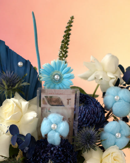 Pearls and Petals new born baby flower arrangement with blue blooms in a woven vase from Whimsy Flowers Abu Dhabi.